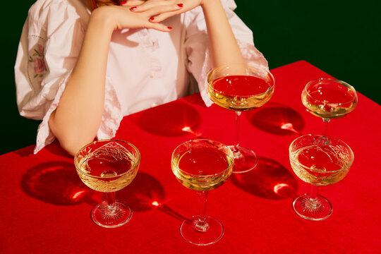 Cropped image of woman in white dress sitting at the table with champagne glasses on red tablecloth over green background