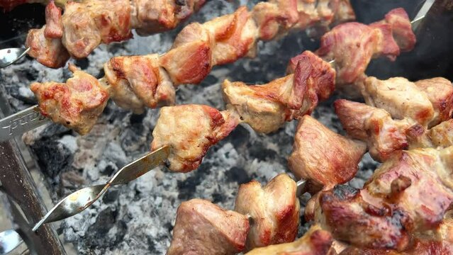 Close-up of grilling tasty dish on barbecue. Process of cooking yummy shashlik in nature. Delicious food on metal skewer in bbq. Time to picnic concept. Street food. Food festival. Pork at the stake.