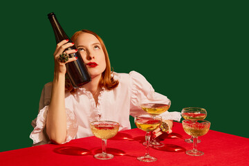 Young redhead girl in festive white dress sitting at the table with champagne over green background. Hangover