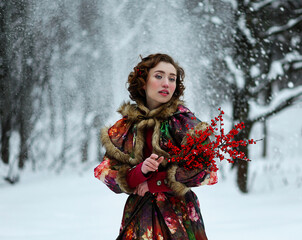Beautiful young woman in red historical dress with red berries in winter forest. Traditional...