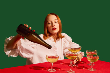 Young redhead girl in festive white dress sitting at the table with champagne over green background. Degustation