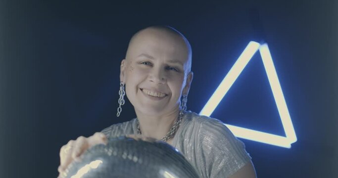 Slow motion portrait of beautiful young woman dancing with glitterball in darkness with neon light flashes illuminating dancer. People and disco concept.