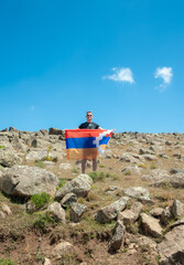 a young handsome man holds in his hands the flag of the unrecognized republic of Nagorno-Karabakh or Artsakh, standing in a large steppe with piled large stones. Support for Artsakh