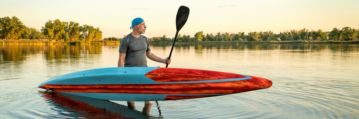 senior male paddler with a long and narrow racing stand up paddleboard on a calm lake at sunset,...