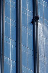 Worker cleaning glass wall at high rise building.