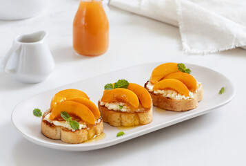 Peach Crostini with crumbled cheese, honey and mint. White background, selective focus.