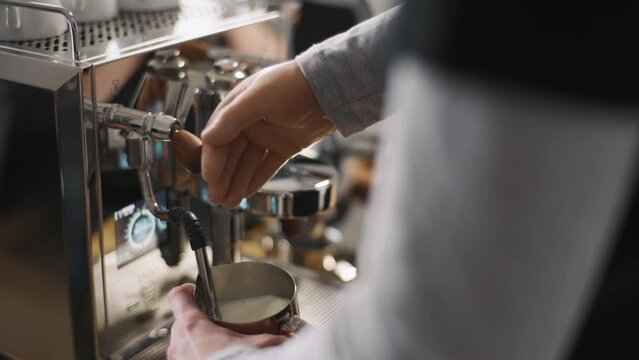 Disabled man with silicone prosthesis hand, barista without arm working in cafe steaming milk in coffee machine pitcher. Physical disability people at work, inclusion and inclusiveness concept