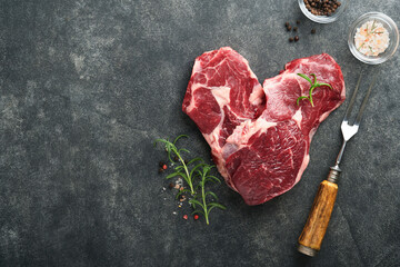 Raw beef steak. Marbled raw fresh Ribeye steak in heart shape with rosemary, salt and pepper on...