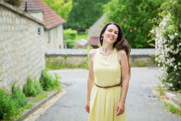 Fototapeta premium Lifestyle portrait of young stylish woman with long brunette hair walking on the street in old town, wearing yellow dress