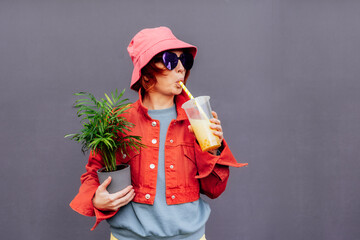 Hipster fashion woman in bright clothes, heart shaped glasses, bucket hat drinking fruity sugar...