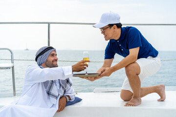 Asian man waiter serving fruit juice to Arab businessman passenger while luxury catamaran boat...
