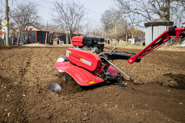 Farmer man plows the land with a red cultivator preparing the soil for sowing.
