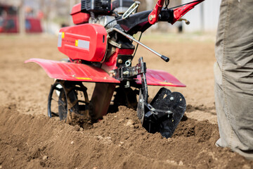 Farmer man plows the land with a red cultivator preparing the soil for sowing.
