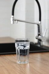 Transparent glass of clean filtering water on wooden table in kitchen interior. Tap with purified water with an osmosis system of the home kitchen sink