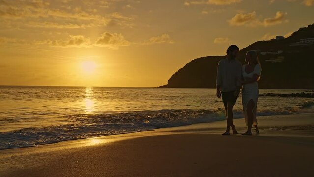 Young attractive couple walking on an island beach while holding hands at sunset in slow motion