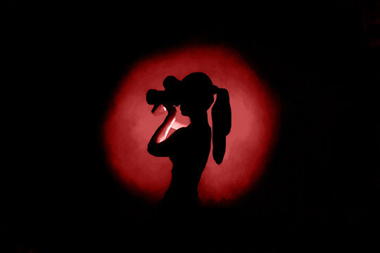 Center red light silhouette on black background and lady photographer with camera taking photos. Concept of art photography. Dark picture at website, avatar, Surreal dark  abstract backdrop