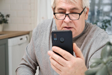 Hoary old man looking shouting to web camera, holding phone talking with clients online. Senior...