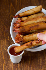The woman dips the shrimp roll into the sweet and sour sauce. Homemade Chinese recipe.