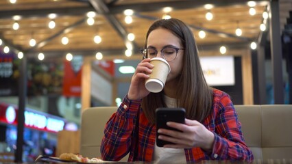 A young woman eats pizza in a cafe with a phone in her hand. A girl in a red shirt and glasses is watching memes on a smartphone.