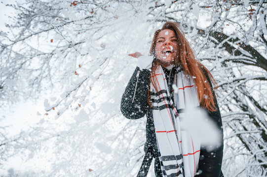 Looking down and throwing the snow. Beautiful young woman is outdoors in the winter forest