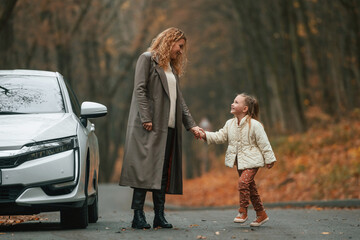 Fototapeta premium Mother with her daughter is outdoors near electric car outdoors