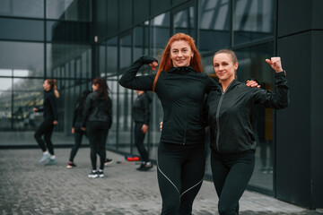 Standing together with arms up, showing muscles, conception of teamwork. Group of sportive women is outdoors