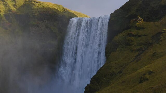 The large Skogafoss waterfall at sunset with a viewpoint at the top and tourists at the bottom in Iceland.