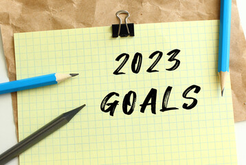 2023 GOALS lettering on a yellow sheet of paper over crumpled kraft paper. Pencils and paper clip.