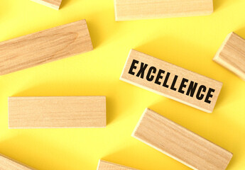 EXCELLENCE text written on a wooden blocks on a yellow background.