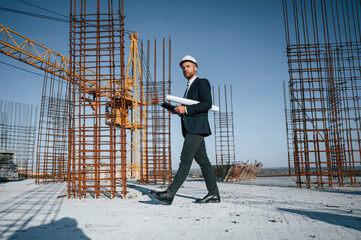 Holding paper with plan and tablet. Businessman in formal clothes is on the construction site at...
