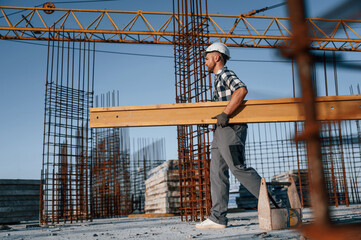 View from the side. Walking and holding wooden plank. Man is working on the construction site at...