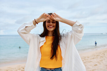 Fototapeta na wymiar Happy woman smile with teeth with long hair brunette walks along the beach in a yellow t-shirt denim shorts and a white shirt near the sea summer journey and feeling of freedom, balance