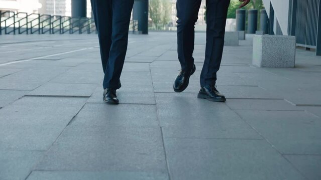 Legs Of Two Colleagues Bankers Going To Work, Front View. Close Up Of Confident Male Bankers In Leather Shoes And A Formal Suit Walking Outdoors Along The Street Of The Business District.