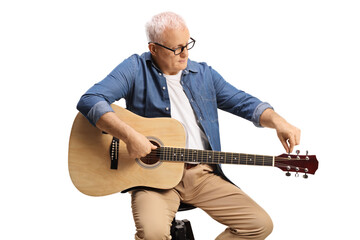 Mature man sitting on a chair and tunning an acoustic guitar