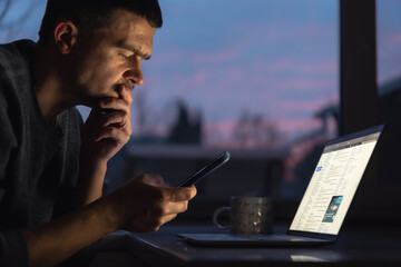 A man works on a laptop early in the morning at dawn in the dark.