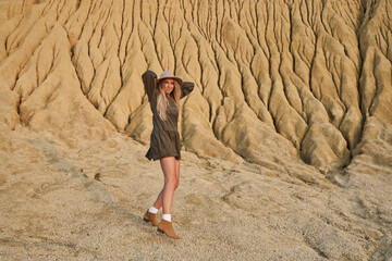 high sand mountain, beautiful natural landscape. a beautiful young woman in a hat and dress of a natural shade dances on a huge sandy mountain