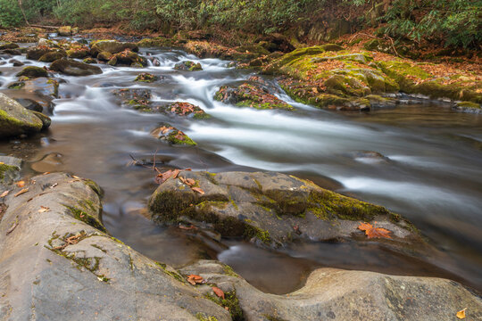 Oconaluftee River in Smoke Mountains of NC silky water cascading over, and around large boulders near Cherokee UDA fall color in background long exposure horizontal photo