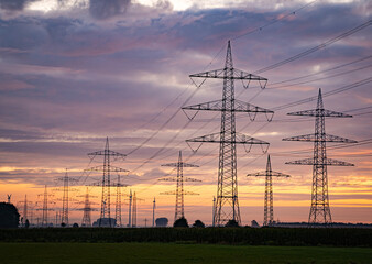 Strommasten mit Stromkabeln vor der untergehenden Sonne mit Wolken, Farbenspiel.