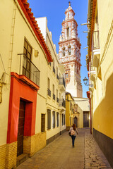 Woman strolling through the narrow streets of the city of Ecija with the impressive church tower in the background.