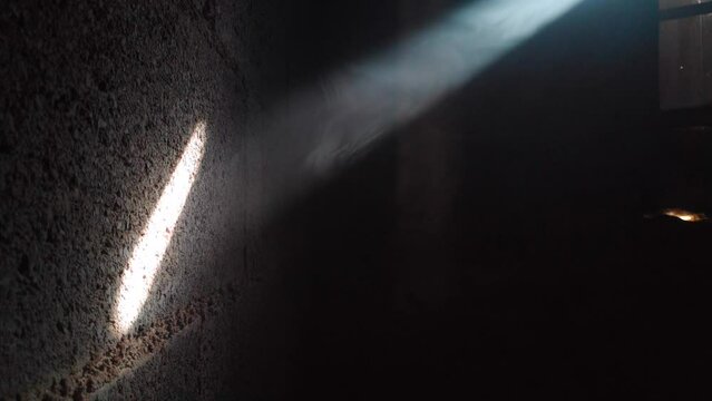 Light beams from a broken shutter entering a smoky room and hitting a cinder block wall.
