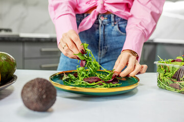 Woman is preparing salad from vegetables and spring mix in kitchen. Close up