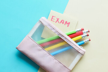 exam word in a sticky note and pencils on color background 