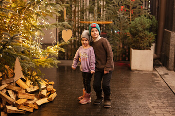 Fototapeta na wymiar Brother with sister having fun near illuminated Christmas tree outdoor in evening.