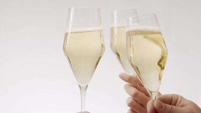 Crop people toasting with champagne glasses. Crop unrecognizable people clinking elegant crystal glasses of champagne against white background during festive event