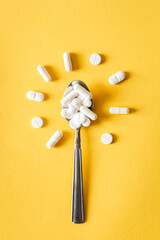 White pills in spoon in the shape of a flower on a yellow background, flat lay.