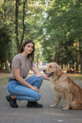 Young beautiful dark-haired girl in a summer park with a golden retriever.