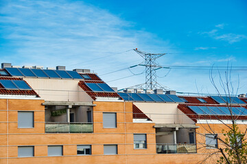 Solar panels on the roof of some houses with bright blue sky and a high voltage tower in the background.