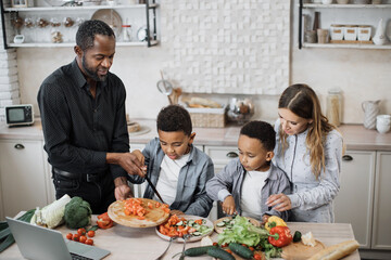 Loving mom, dad and small sons kids cooking dinner together. Happy young parents teaching little preschooler boys to chop vegetables with knife preparing salad for lunch together.