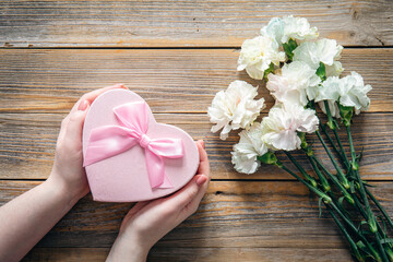 Bouquet of flowers and heart shaped gift box on wooden background, flat lay.
