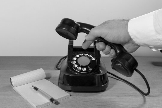 Old telephone set on a wooden table, Man's hand dialing a phone number on a phone disk. retro installation. Black and white